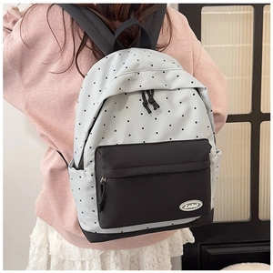 Detailed back view of a white polka dot backpack with black straps worn by a model