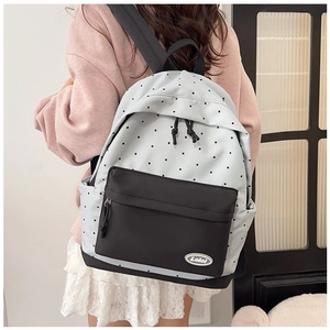 Detail of light blue polka dot backpack with black front pocket and logo plaque