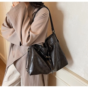 Detail shot of a large black leather tote bag with glossy finish and gold metal hardware