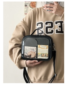 Model wearing a black square crossbody bag with a transparent window and adjustable strap