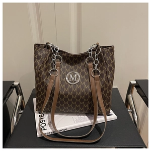 Close-up of a brown tote bag with M-pattern print and silver chain strap on a chair