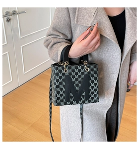 Detail of a black leather handbag featuring grey M-pattern print and a large M logo patch