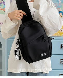 Detail of black crossbody chest bag with decorative zipper and mini sneaker charm