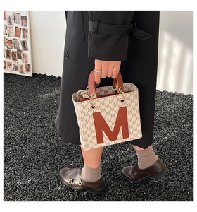 Chic beige canvas shoulder bag with brown leather M letter pattern in a stylish setting