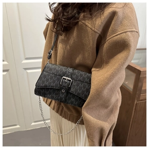 Close-up of black crossbody bag with silver buckle and M-letter pattern on a model