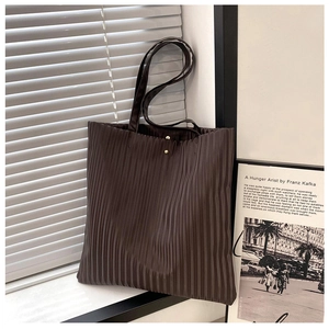Detail of dark brown pleated tote bag with golden magnetic snap and sleek shoulder strap