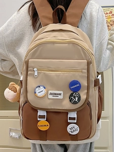Detail of a beige and brown school backpack with cute badges and a small plush bear charm