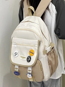 Detail view of cream and khaki color-block student backpack with decorative fashion badges