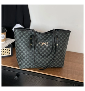 Gros plan sur le sac cabas noir avec motif jacquard M et pendentif nœud doré