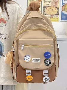Detail of color-block student backpack with decorative badges and plush bear pendant