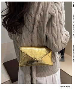 Détail du sac enveloppe plissé doré métallisé avec bandoulière chaîne et pull beige douillet