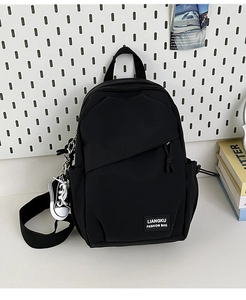 Detail of black nylon backpack featuring a brand logo patch and a mini sneaker charm