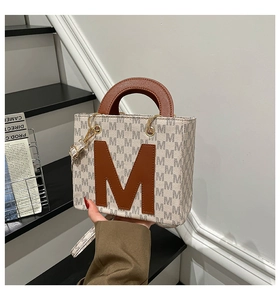 Detail of the monogrammed pattern and central leather M applique on a cream tote bag