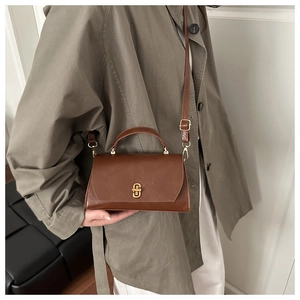 Detail view of retro brown crossbody bag with gold metal buckle on olive green trench coat
