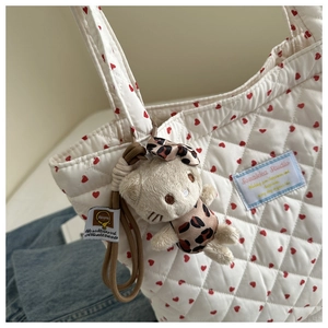 Détail d'un cabas matelassé blanc à cœurs rouges avec un pendentif en peluche
