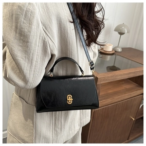 Close-up of minimalist black leather crossbody bag with elegant gold oval metal lock