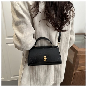 Detail showing the vintage gold clasp and glossy black leather of the square bag