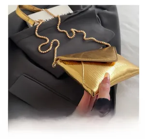 Détail du sac enveloppe doré avec texture ondulée métallique et bandoulière chaîne