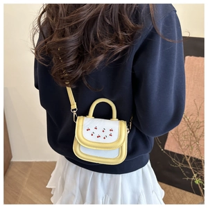 Detail view of the cherry embroidery on a yellow and white leather crossbody bag