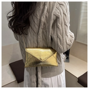 Détail du sac enveloppe doré métallisé avec texture plissée fine et bandoulière chaîne