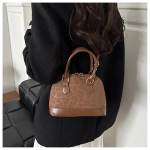 Brown shell bag with leopard print texture and gold hardware on model in a modern room