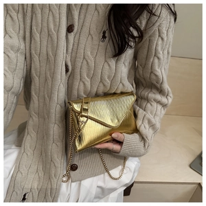 Détail de la pochette dorée métallisée avec texture verticale fine et bandoulière chaîne