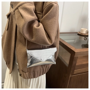 Détail du sac enveloppe argenté avec chaîne dorée et texture ondulée raffinée