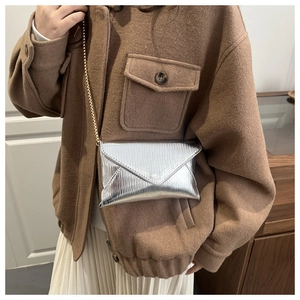 Détail du sac enveloppe argenté avec texture ondulée et bandoulière chaîne dorée