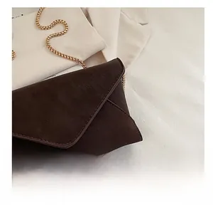 Nahaufnahme einer dunkelbraunen Wildleder-Umschlagtasche mit goldener Kette und Nähten