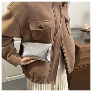 Détail de la pochette enveloppe argentée avec texture plissée et fine chaîne dorée