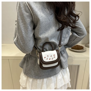 Detail of a cherry print crossbody bag featuring brown leather trim and golden metal clasp