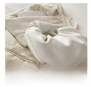 Détail du sac à main plissé en cuir blanc avec poignée nouée sur tissu beige