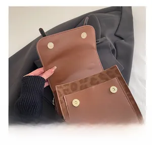 Close-up of brown leather bag featuring dual magnetic gold snaps and suede interior lining