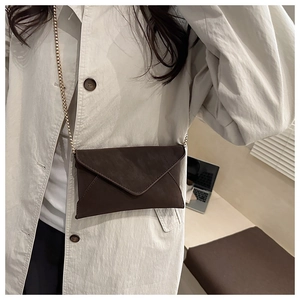 Detail der dunkelbraunen Leder-Umschlagtasche mit goldener Kette an einem Model