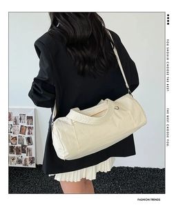 Close-up of cream-colored nylon cylinder bag with adjustable strap worn by model
