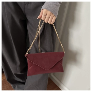 Detail der weinroten Wildleder-Umschlagtasche mit eleganter goldener Kette zum Tragen
