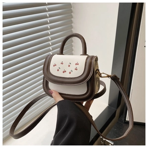 Close-up of cherry print crossbody bag featuring golden hooks and brown leather straps