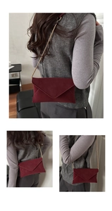Detail der weinroten Umschlagtasche mit Goldkette, getragen zu einer grauen Weste