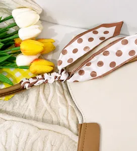 Close-up of a white leather tote bag with brown trim and decorative polka dot scarf