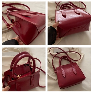 Detail view of the red glossy leather bag showing its side, base, and metal zipper closure