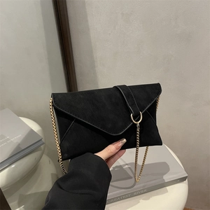 Minimalistische schwarze Umschlag-Kettentasche aus mattem Wildleder vor grauem Hintergrund