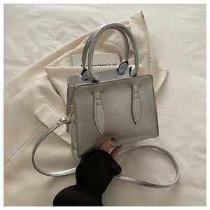 Detail view of silver pleated faux leather texture and golden hardware on small square bag