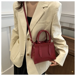 Detail of red glossy leather handbag with leaf stitching worn with beige corduroy blazer