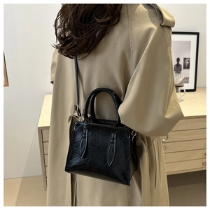 Detailed back view of a black glossy square crossbody bag worn with a stylish trench coat