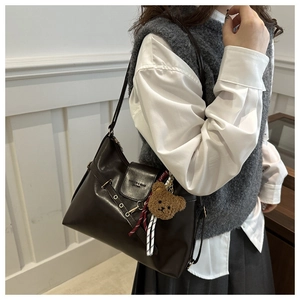 Détail du sac cabas en cuir marron foncé avec charm d'ours en peluche et boucle en métal