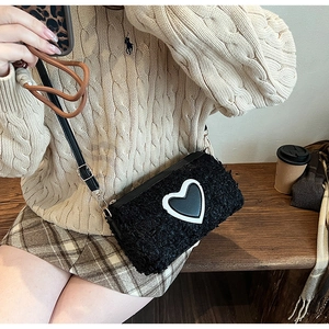 Dettaglio della borsa a tracolla in pile nero con patch a cuore e cinturino in pelle
