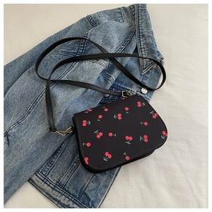 Detail der schwarzen Satteltasche mit Kirschprint und goldenem Verschluss auf Denim