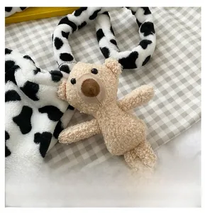 Detail of soft plush bear pendant with cow print strap on checkered background