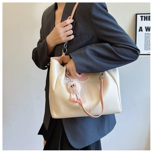 Close-up of stylish beige tote bag with pink straps and a cute monster pendant accessory