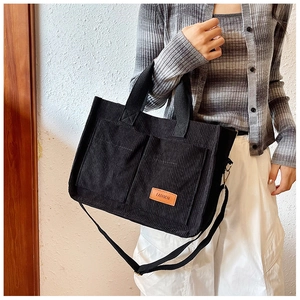 Detail of black corduroy tote bag showing front pockets and fashion leather label